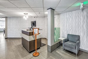 Un mostrador de recepción con un letrero, una silla tapizada gris y una pared con textura.