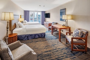 A hotel room with two beds, a desk, a chair, a lamp, and a television.