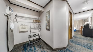 Pasillo de hotel con perchero, toallero, un cuadro y una puerta que da a un dormitorio.
