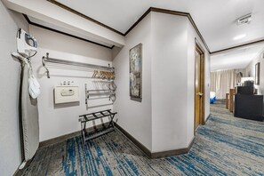 A hotel corridor with a coat rack, a towel rack, a painting, and a door leading to a bedroom. - The Voyager Inn (Anchorage)