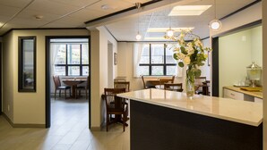 A modern kitchen with a central island, a dining area with wooden chairs, and a large window providing natural light. - The Voyager Inn (Anchorage)