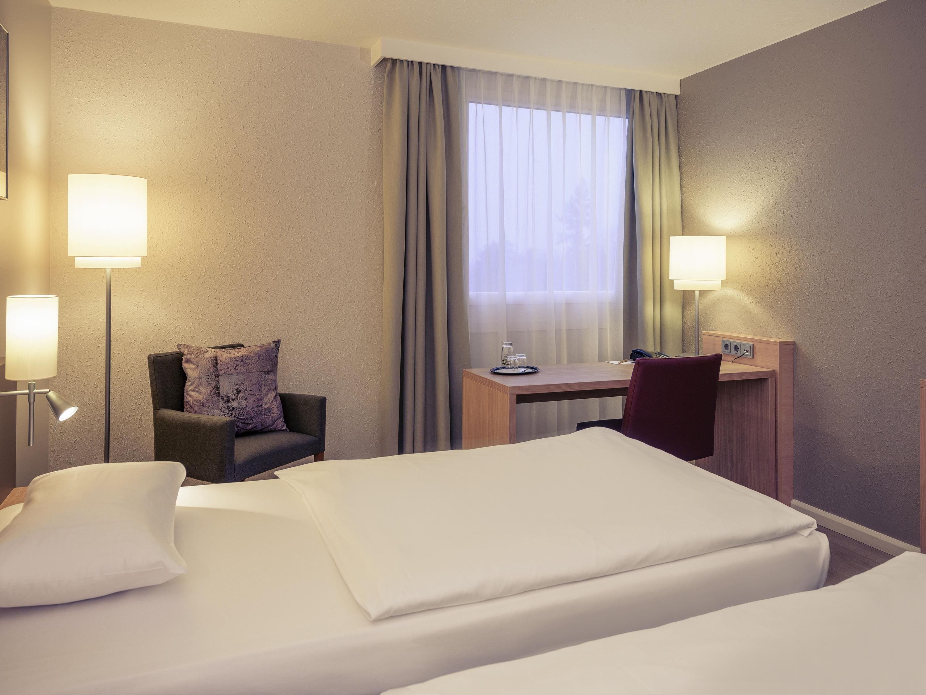 A hotel room with two beds, a desk, a chair, and two bedside lamps.