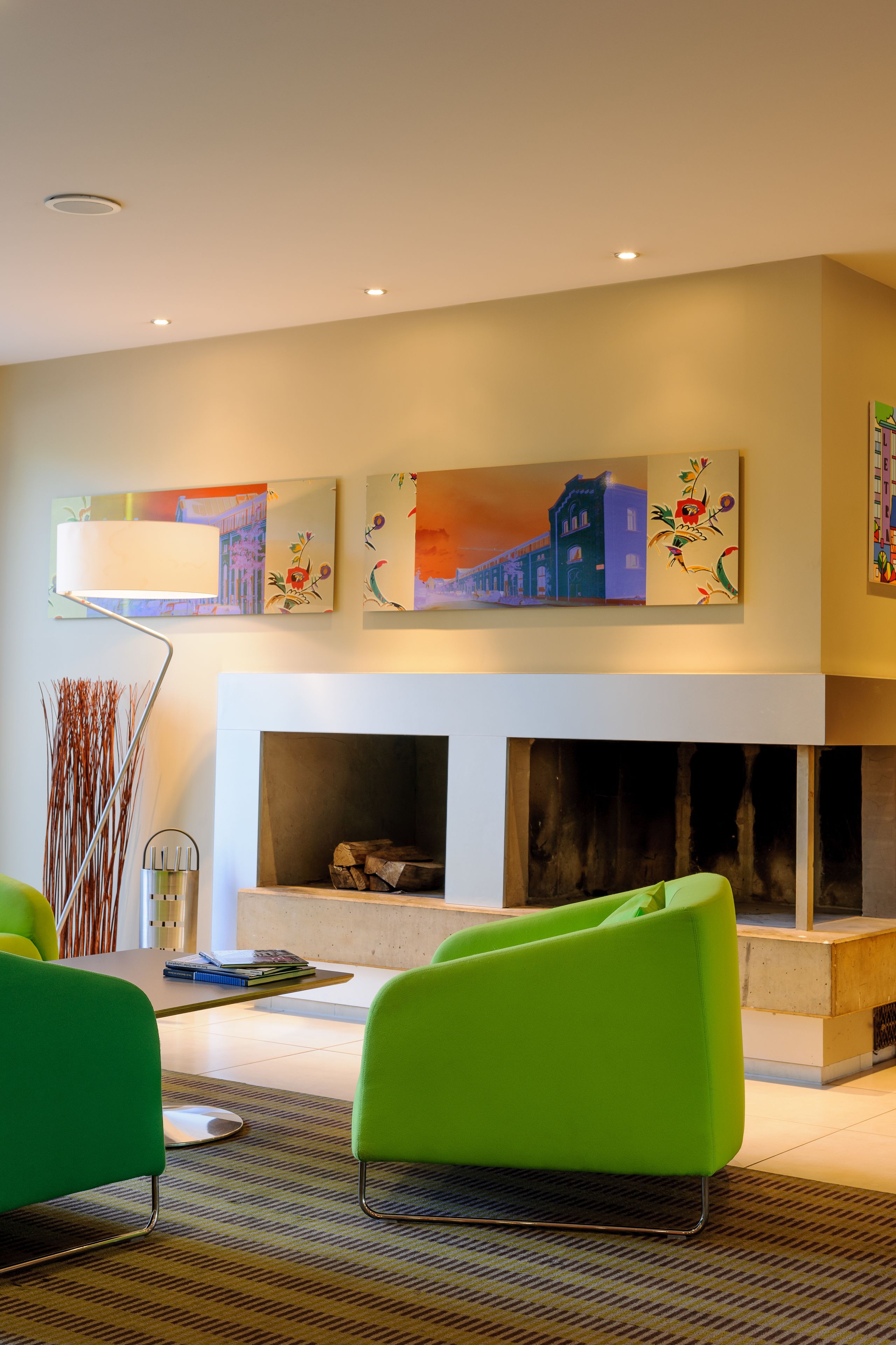 Een moderne woonkamer met een open haard, groene fauteuils en kunstwerken aan de wanden.