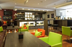 Zona de bar moderna con barra, asientos con sillas verde brillante y una variedad de botellas y vasos en estanterías.