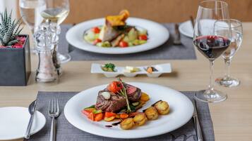A dining table with plates of food, cutlery, and glasses of wine.