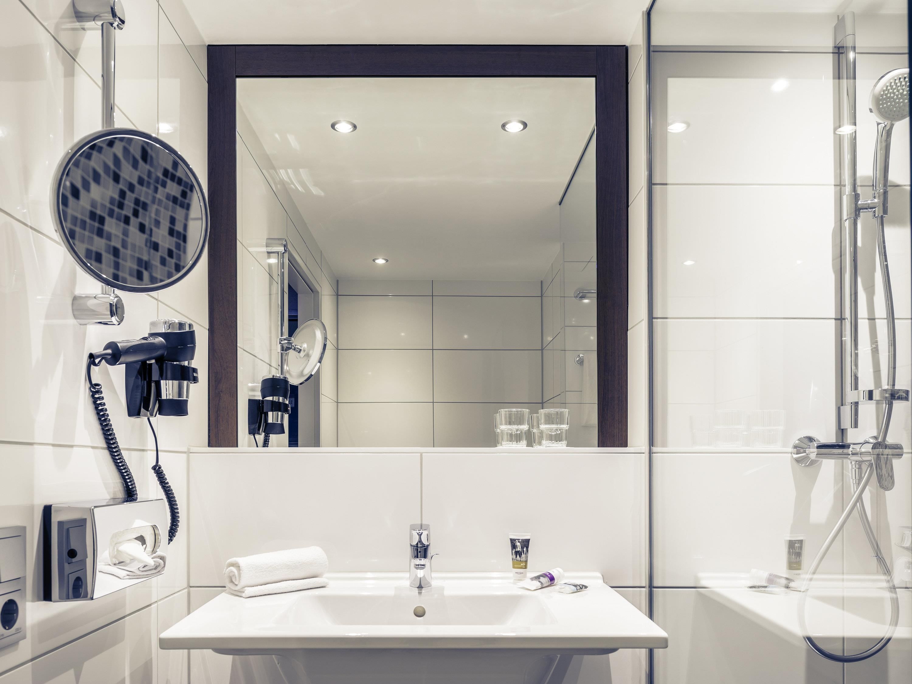 Un baño moderno con un espejo grande, un secador de pelo, una toalla, un lavamanos y una ducha.