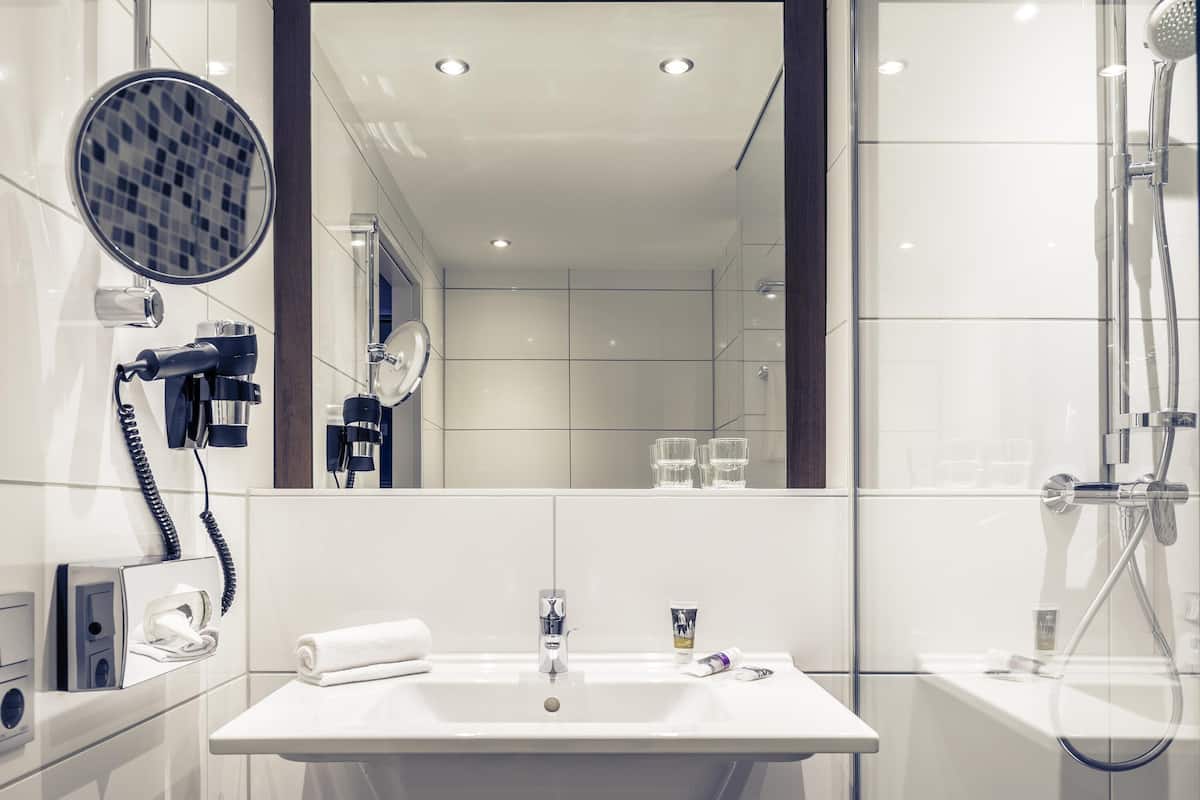 A modern bathroom with a large mirror, a hairdryer, a towel, a sink, and a shower.