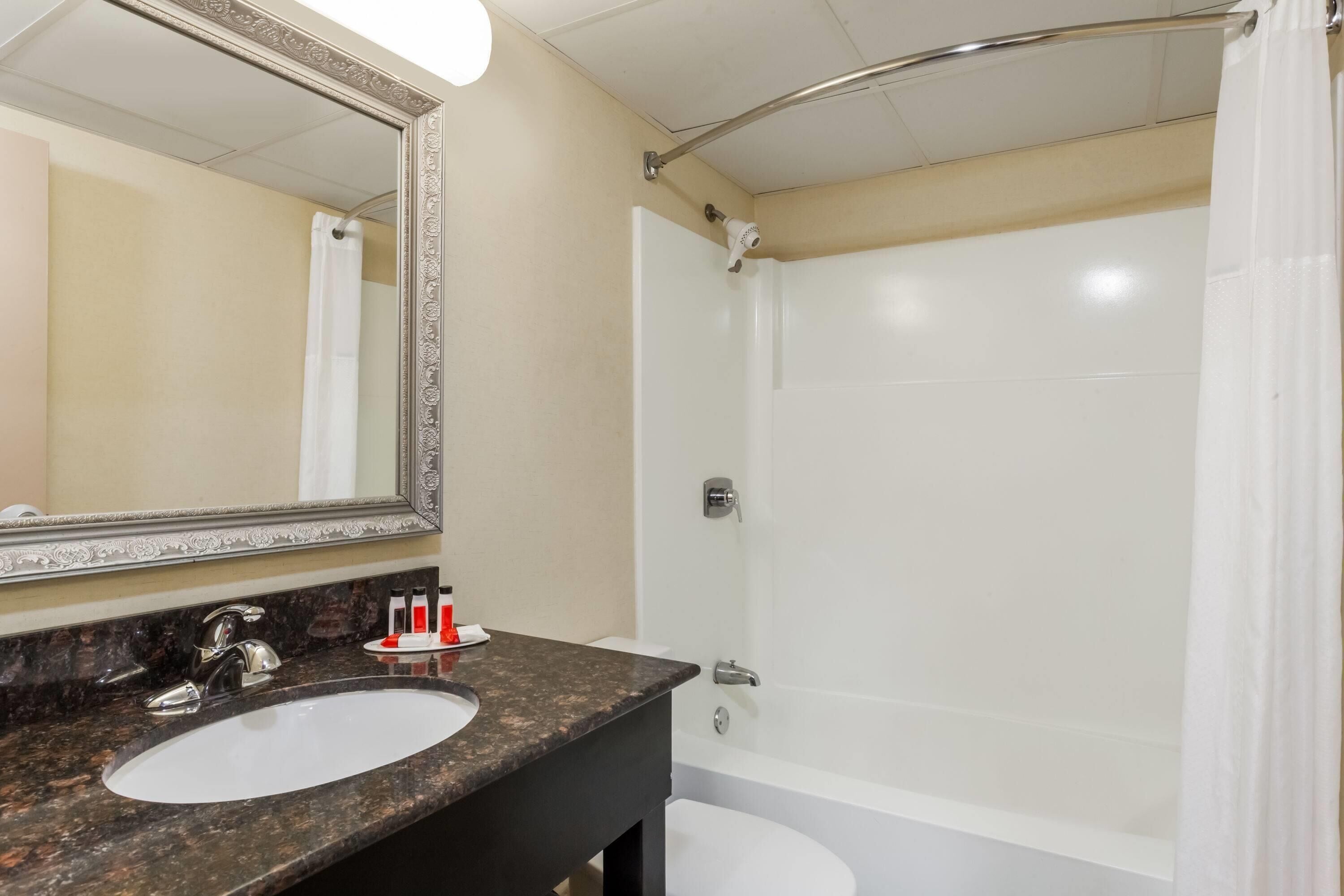 A bathroom with a marble sink, a large mirror, a bathtub, and a shower curtain.