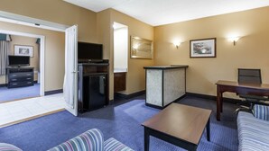 Habitación de hotel con sofá, una mesita, televisor, refrigerador y escritorio con silla.