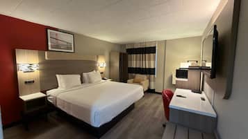 Una habitació d'hotel amb un llit, taules de nit, escriptori amb cadira, televisió i finestra amb cortines.