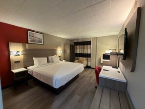 A hotel room with a bed, bedside tables, a desk with a chair, a television, and a window with curtains. - Ramada by Wyndham Newburgh/West Point (Newburgh)