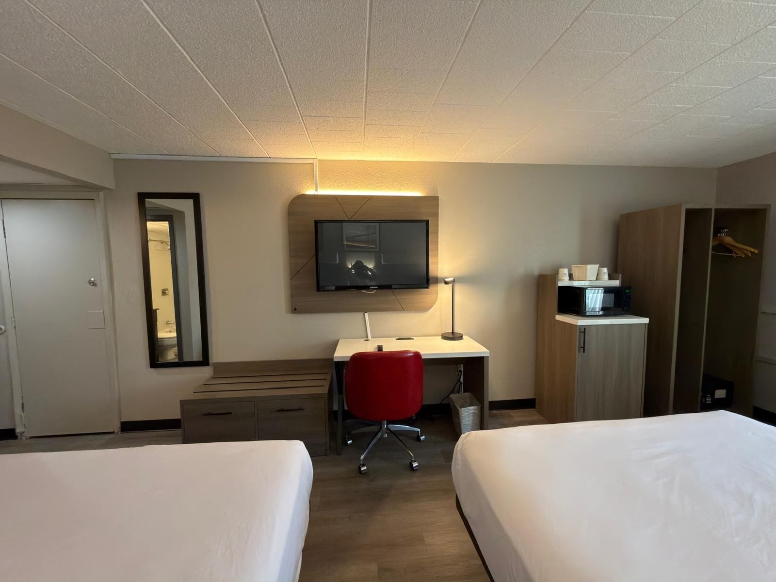 Een hotelkamer met twee bedden, een bureau met stoel, een televisie, een kledingkast en een kleine kitchenette.