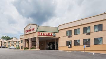 A Ramada hotel with a beige exterior, a green roof, and a parking lot in front.
