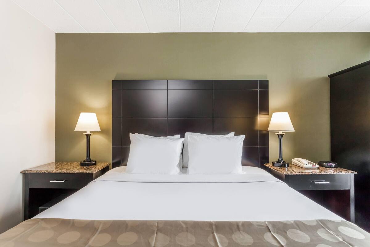 A hotel room with a large bed, two bedside tables with lamps, a telephone, and a dark headboard.