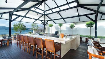 Een terras buiten met een bar, houten stoelen en uitzicht op zee.