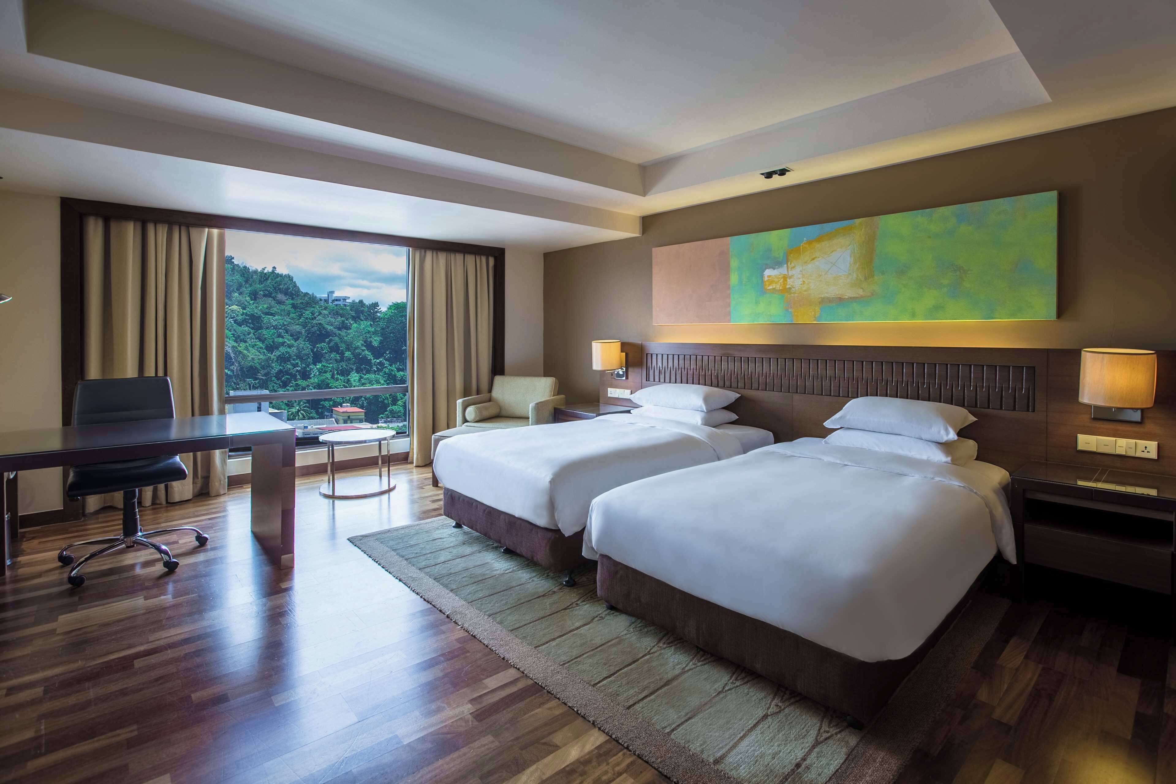 Quarto de hotel com duas camas, uma escrivaninha, uma cadeira, uma janela com cortinas e um quadro na parede.