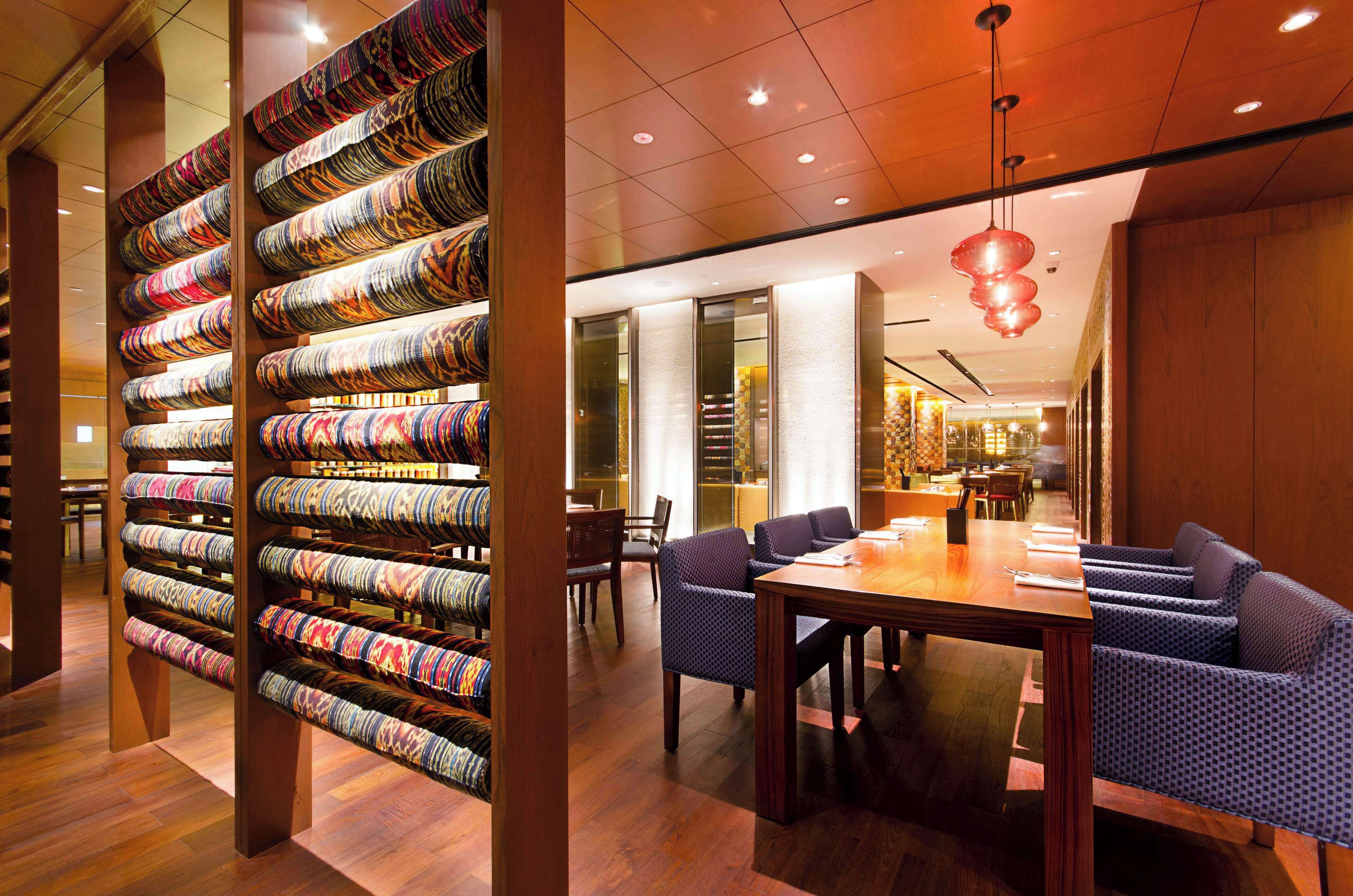 A modern hotel lobby with a seating area, a patterned wall display, and a dining setup.