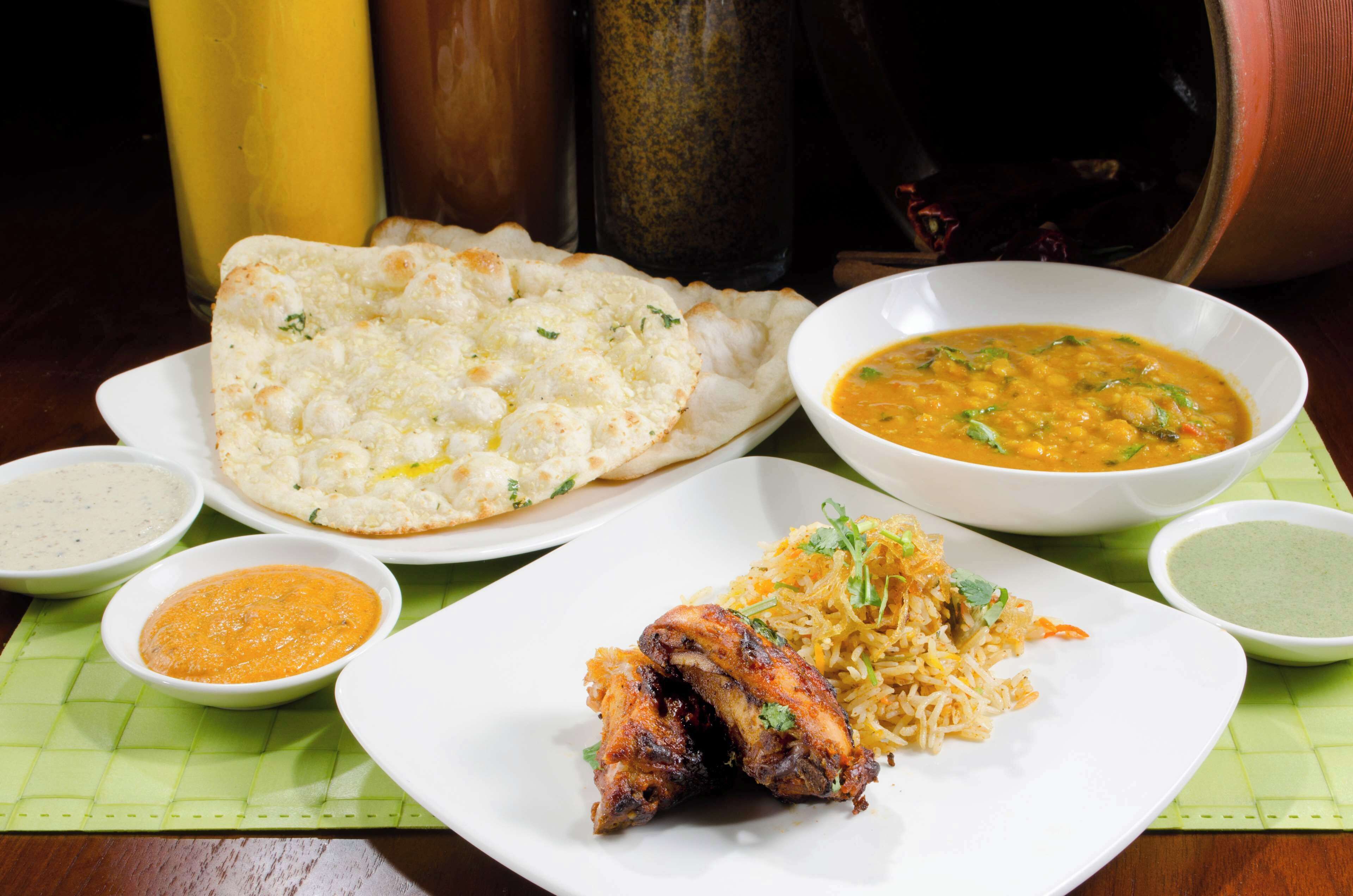 A table with various dishes including naan bread, a bowl of dal, a plate of biryani, and several small bowls of sauces.