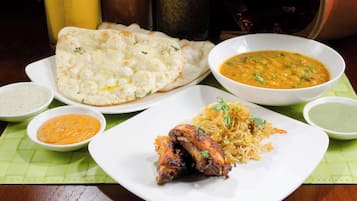 A table with various dishes including naan bread, a bowl of dal, a plate of biryani, and several small bowls of sauces.