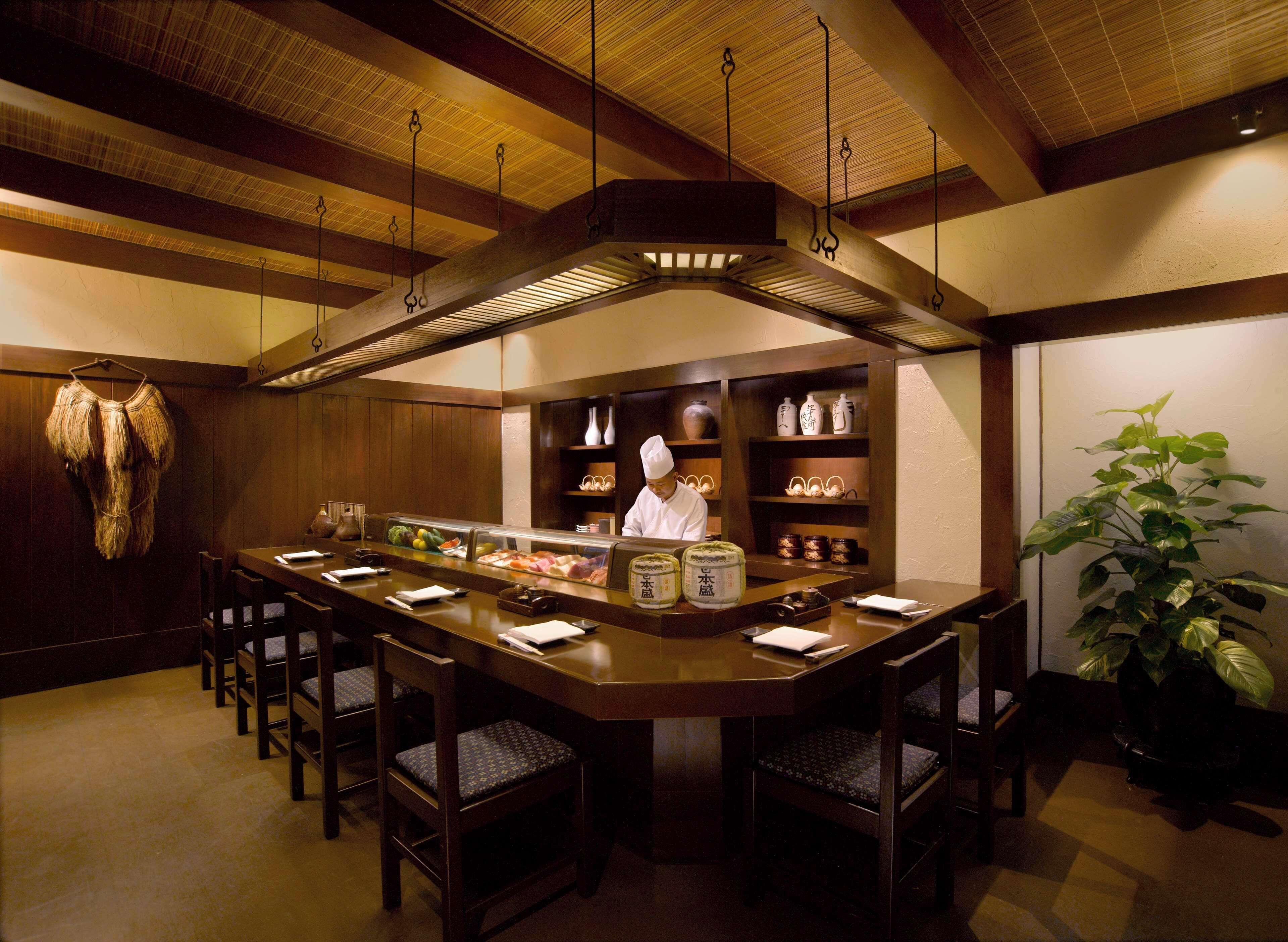 A restaurant with a wooden interior, a chef at the counter, and several chairs around the dining area.