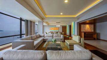 A modern living room with a large sectional sofa, a glass coffee table, and a view of the sea through large windows.