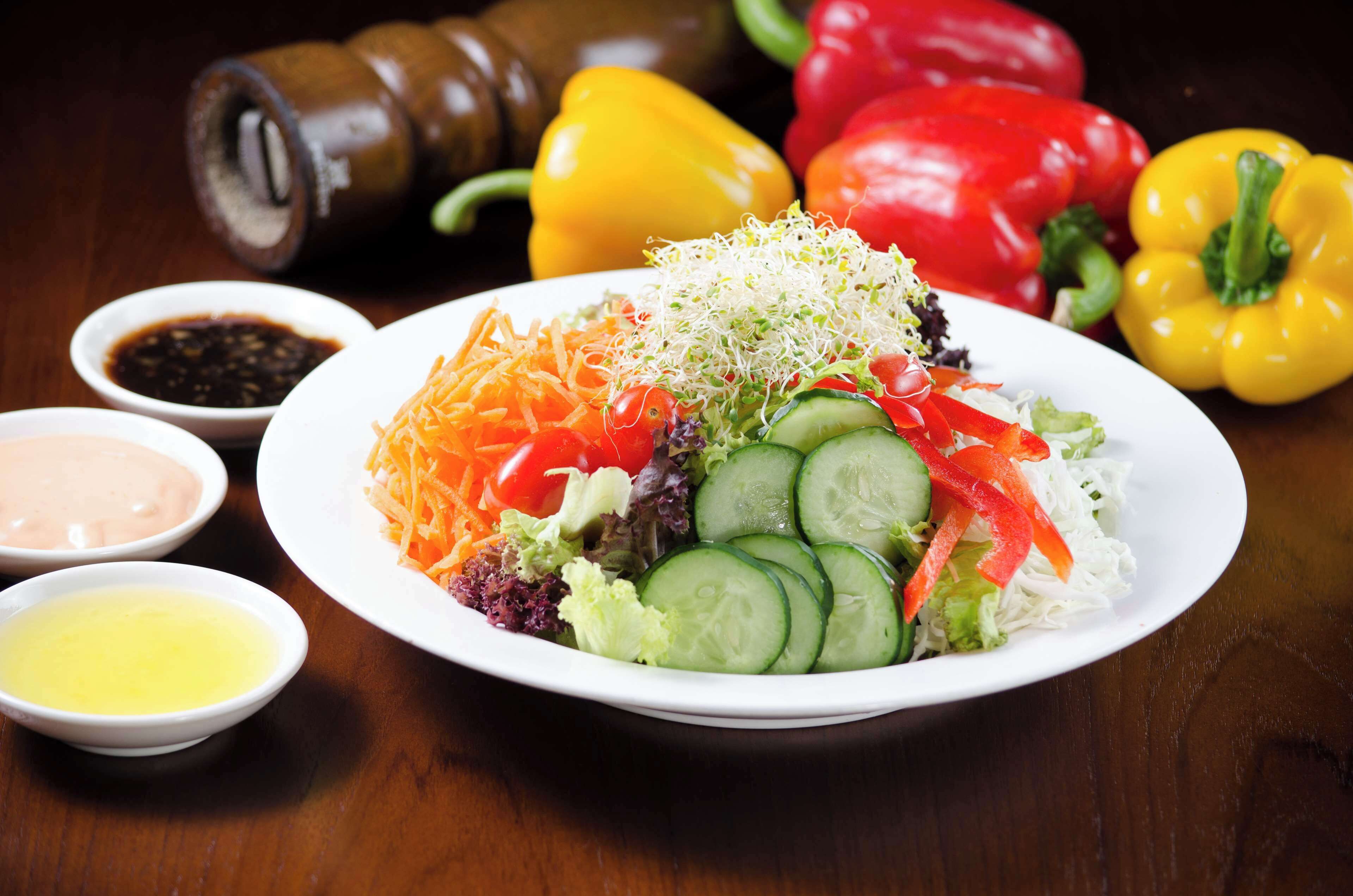 A plate of salad with various vegetables and sprouts, accompanied by small bowls of dressing.