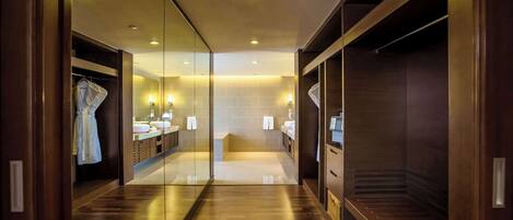 A modern hotel bathroom with a glass partition, wooden flooring, and built-in storage cabinets.