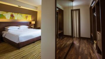A hotel room with a large bed, a wooden floor, a wardrobe, and a painting on the wall.