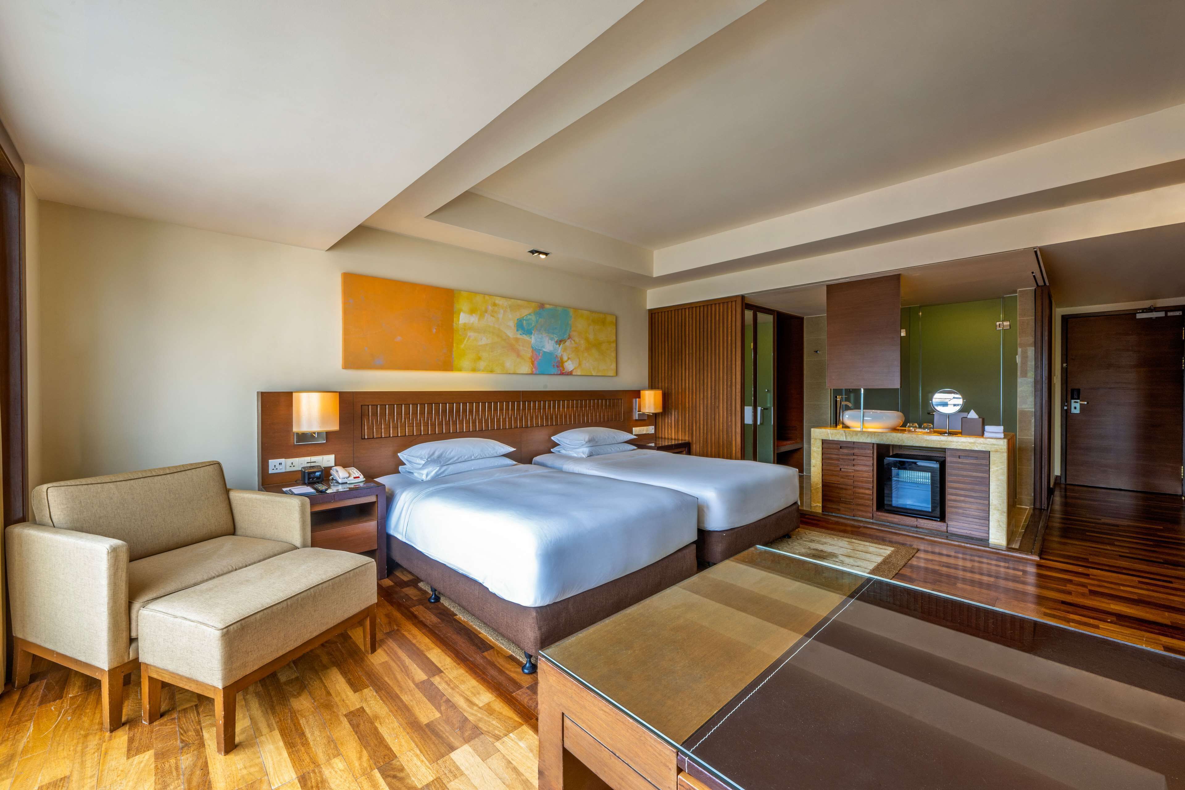 A hotel room with two beds, a sofa, a desk, and a small kitchenette.