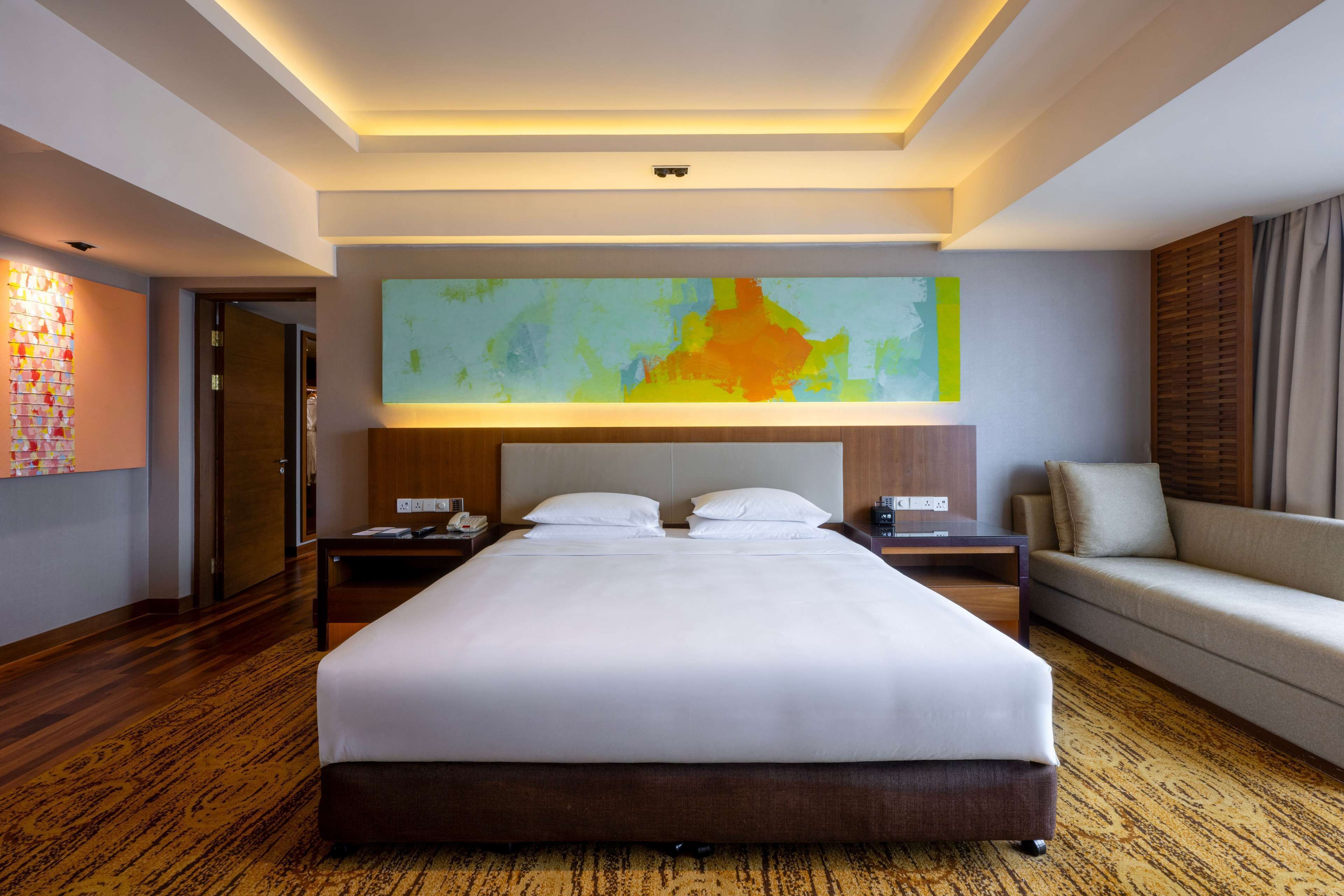 Habitación de hotel con una cama grande, dos mesitas de noche, un sofá y un cuadro abstracto de gran tamaño en la pared.