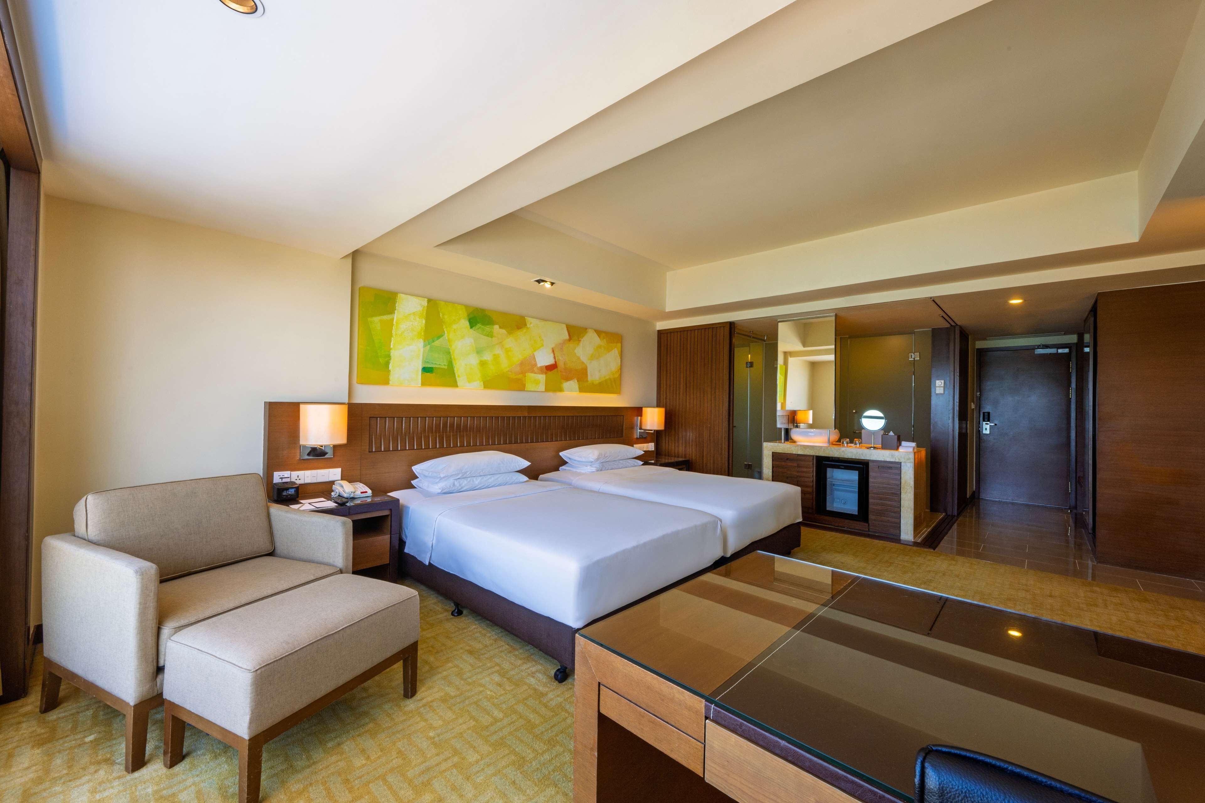 A hotel room with two beds, a desk, a chair, a desk lamp, a nightstand, and a large mirror.