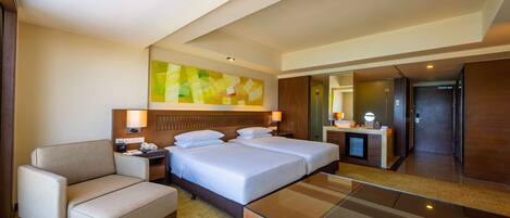 A hotel room with two beds, a desk, a chair, a desk lamp, a nightstand, and a large mirror.