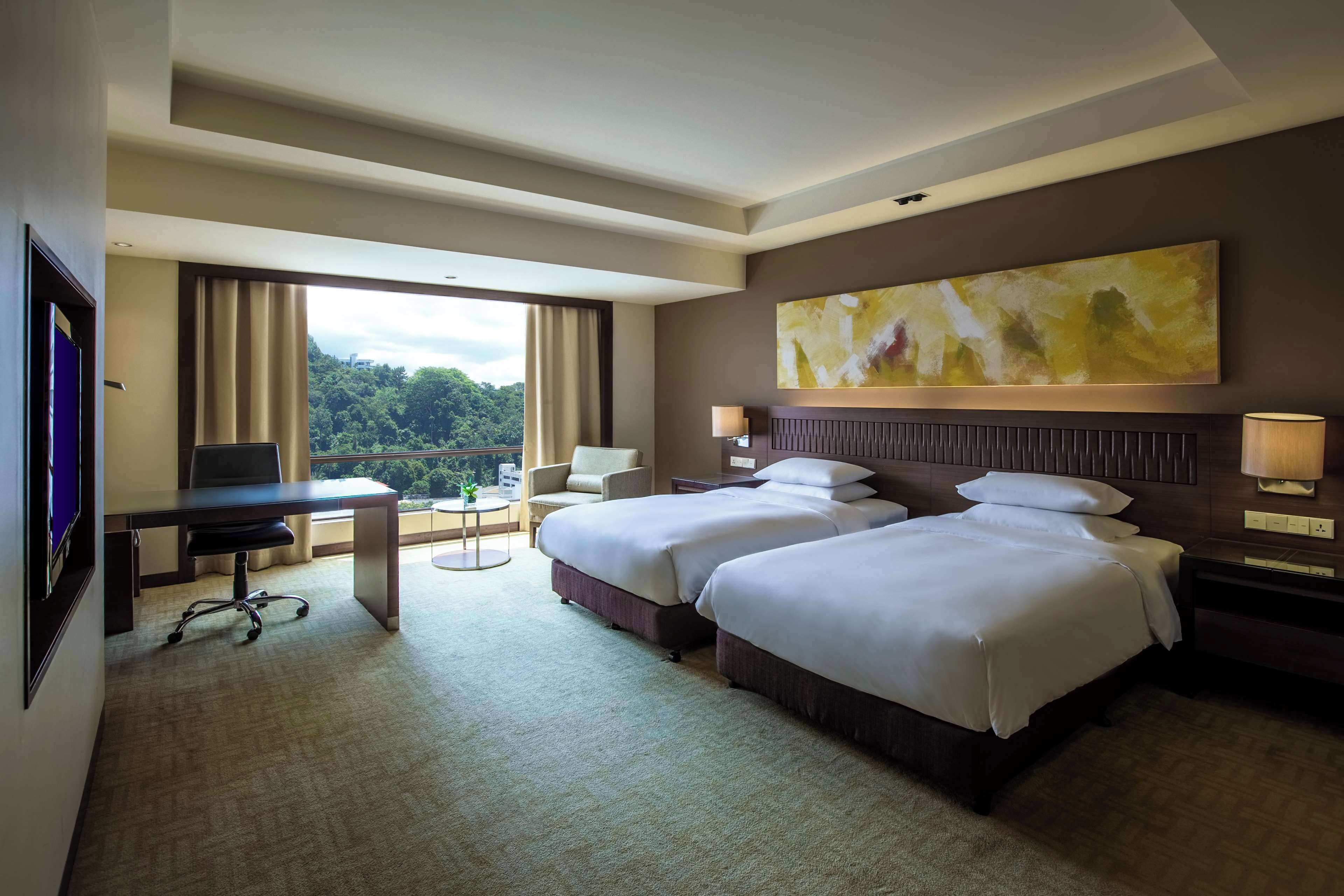 A hotel room with two beds, a desk, a chair, and a large window offering a view of the outdoors.