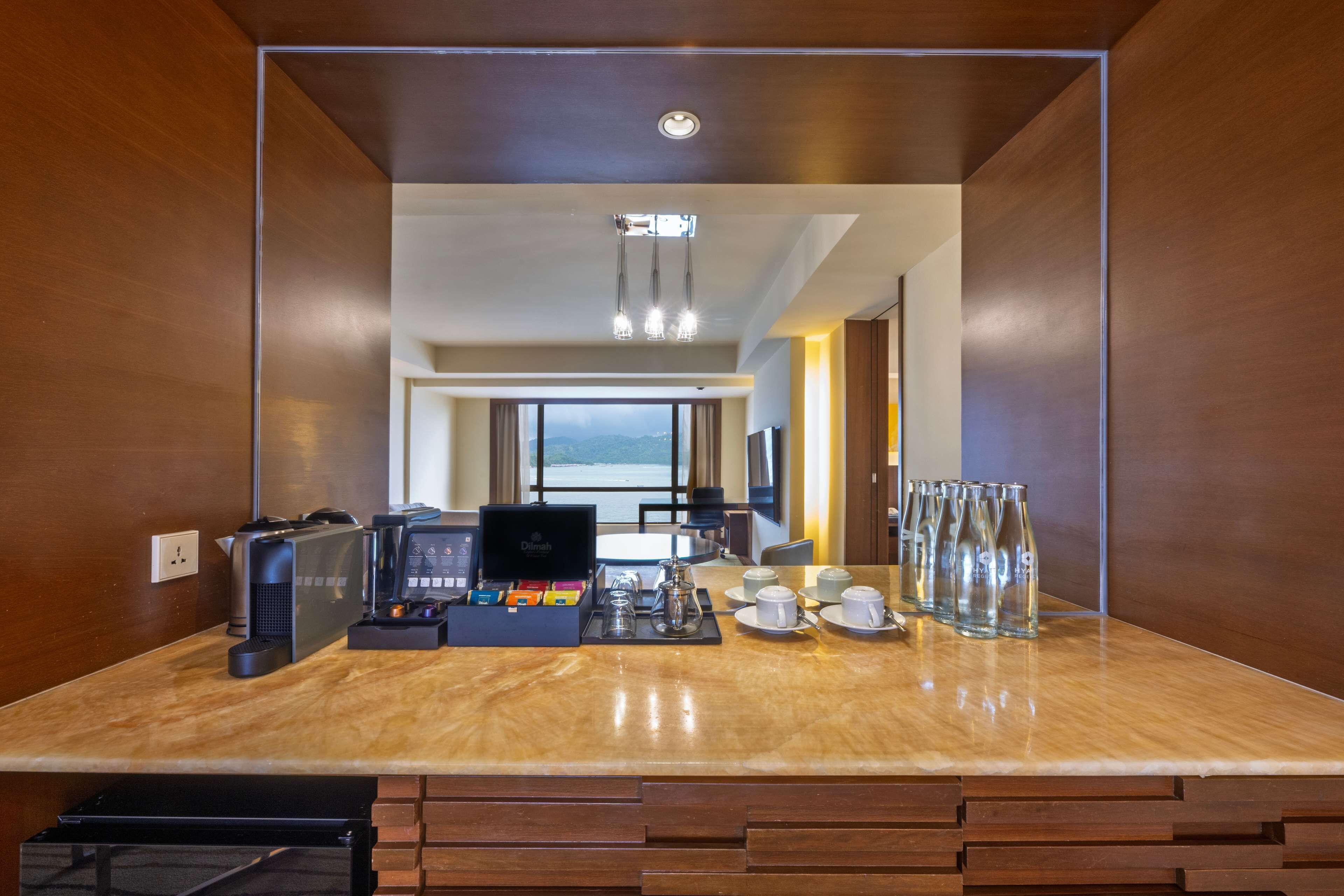 A modern hotel room with a wooden interior, a marble countertop with coffee-making equipment, and a view of the sea through large windows.