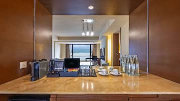 A modern hotel room with a wooden interior, a marble countertop with coffee-making equipment, and a view of the sea through large windows.