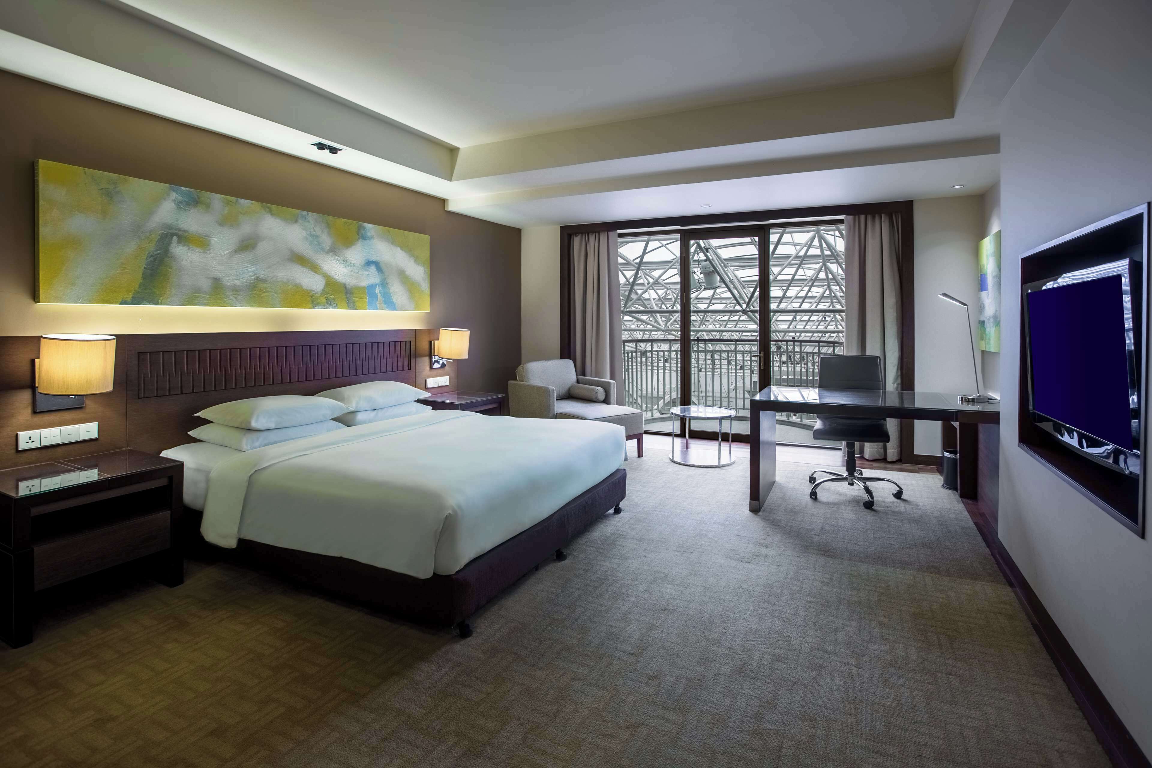 Une chambre d’hôtel avec un lit, un bureau, une chaise et une grande fenêtre.