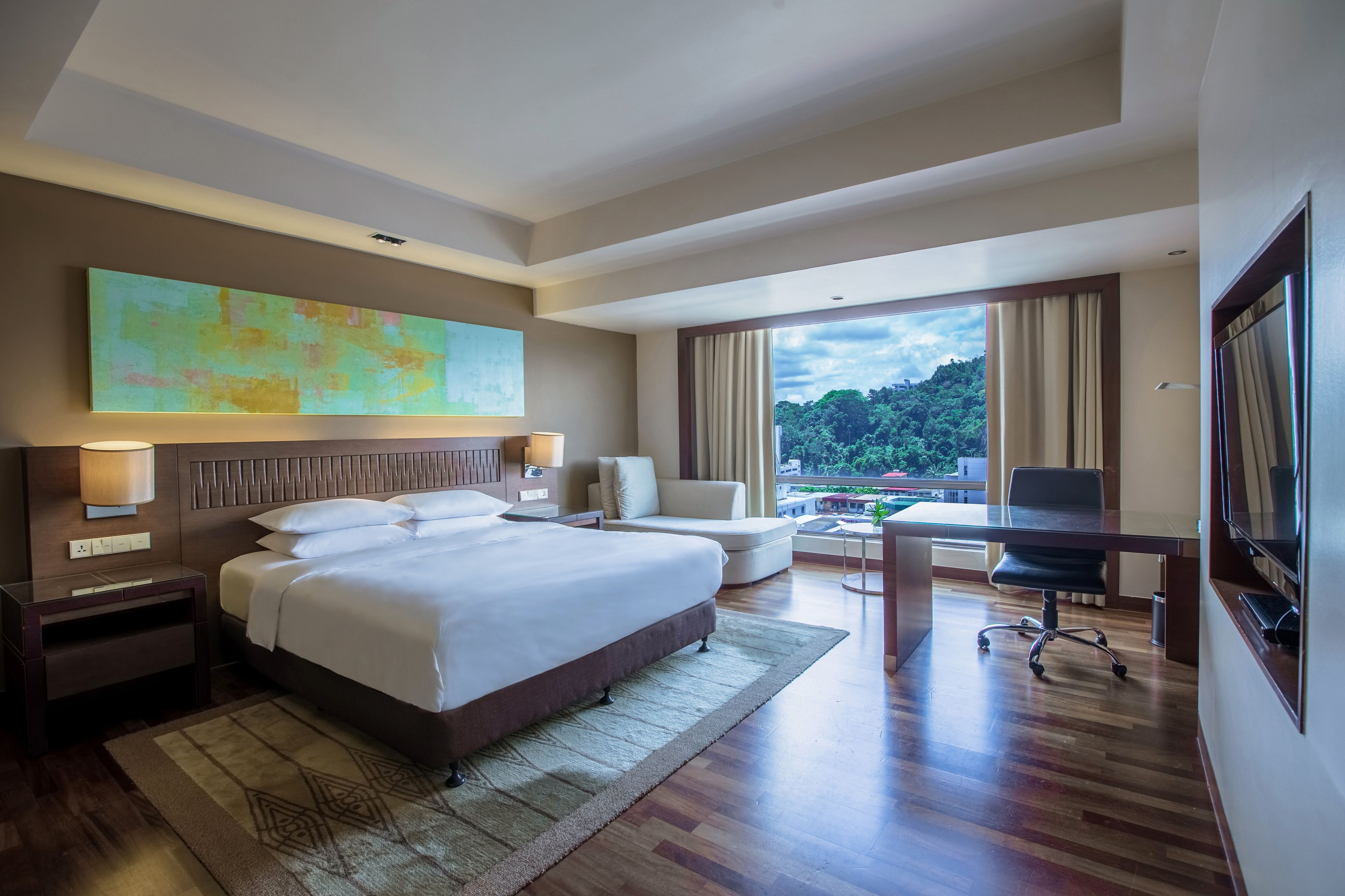 A modern hotel room with a large bed, a desk, and a view of a lush landscape.