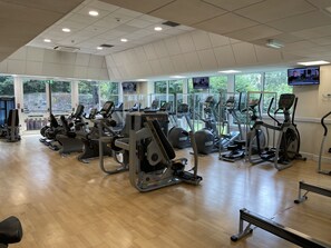Un gimnasio con varias máquinas de ejercicio, ventanas amplias e iluminación empotrada en el techo.