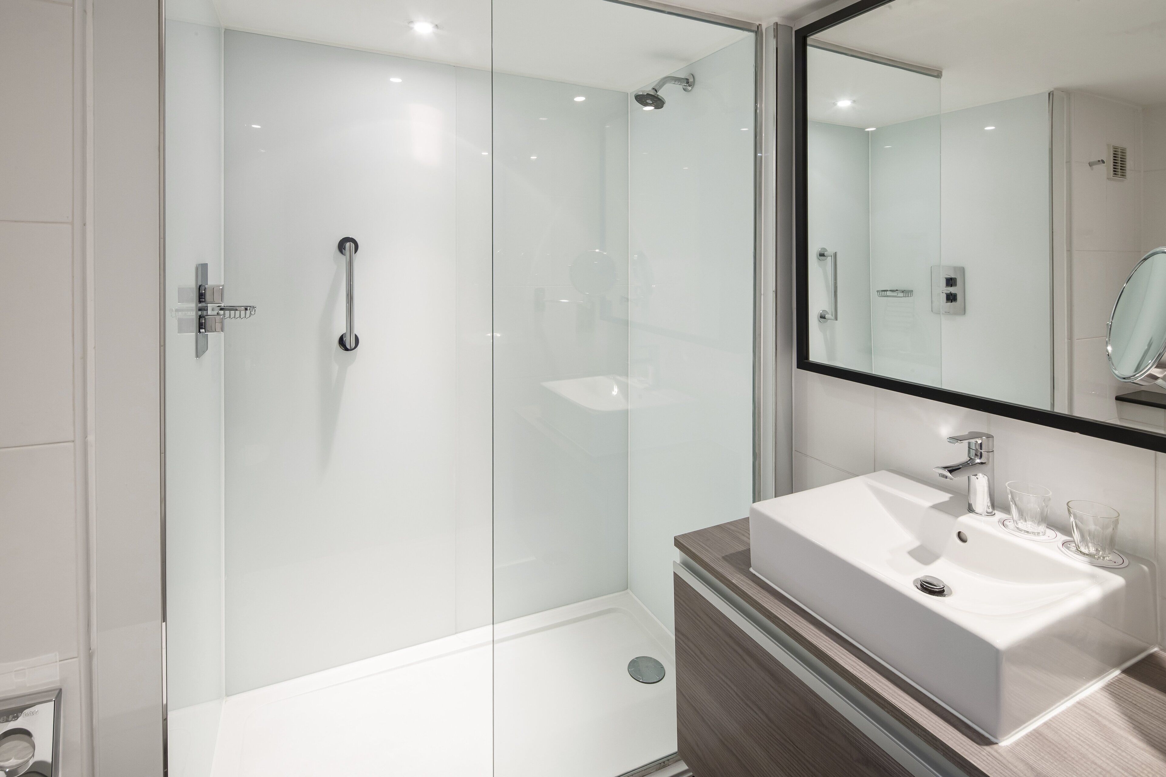 Een moderne badkamer met een douche met glazen wand, een witte wastafel en een grote spiegel.