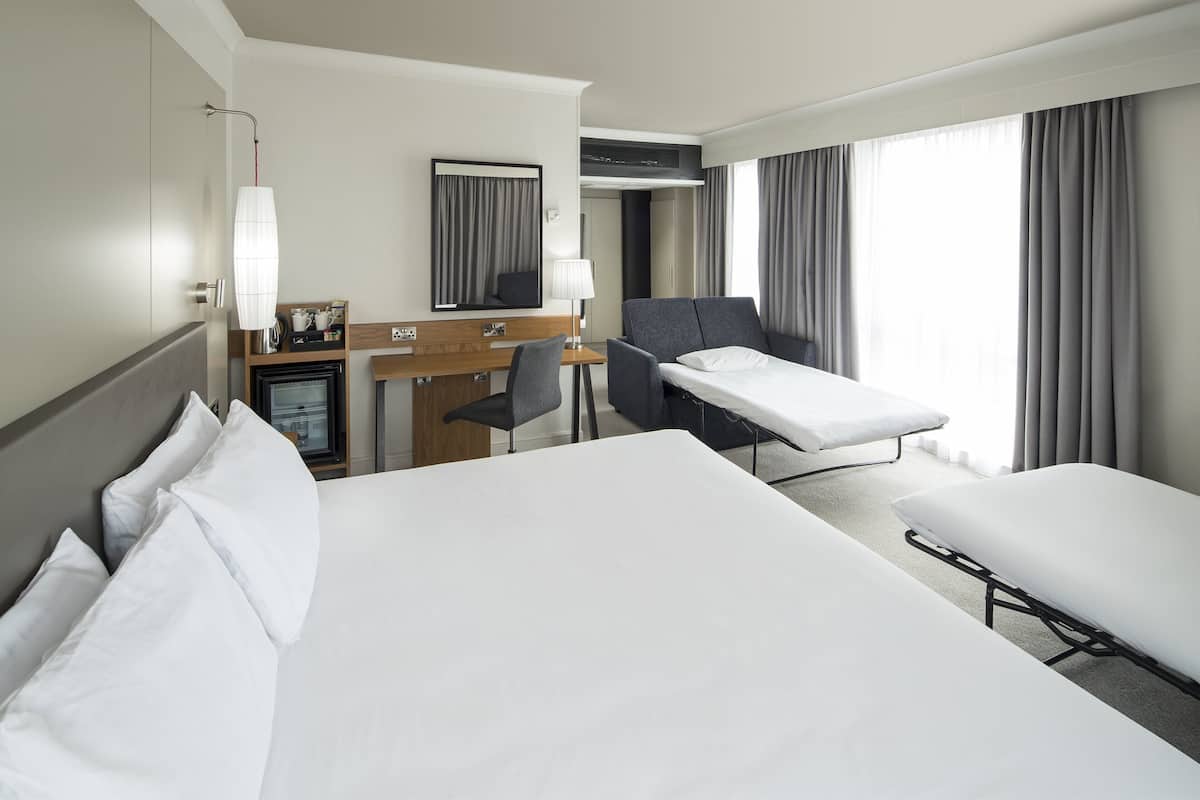 A hotel room with a large bed, a desk with a chair, a small table with a lamp, and a TV.