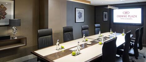 A conference room with a long table, chairs, and a projector screen displaying the Crowne Plaza logo.