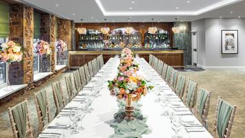 Una larga mesa de banquete decorada con centros de flores, rodeada de sillas con cojines verdes.