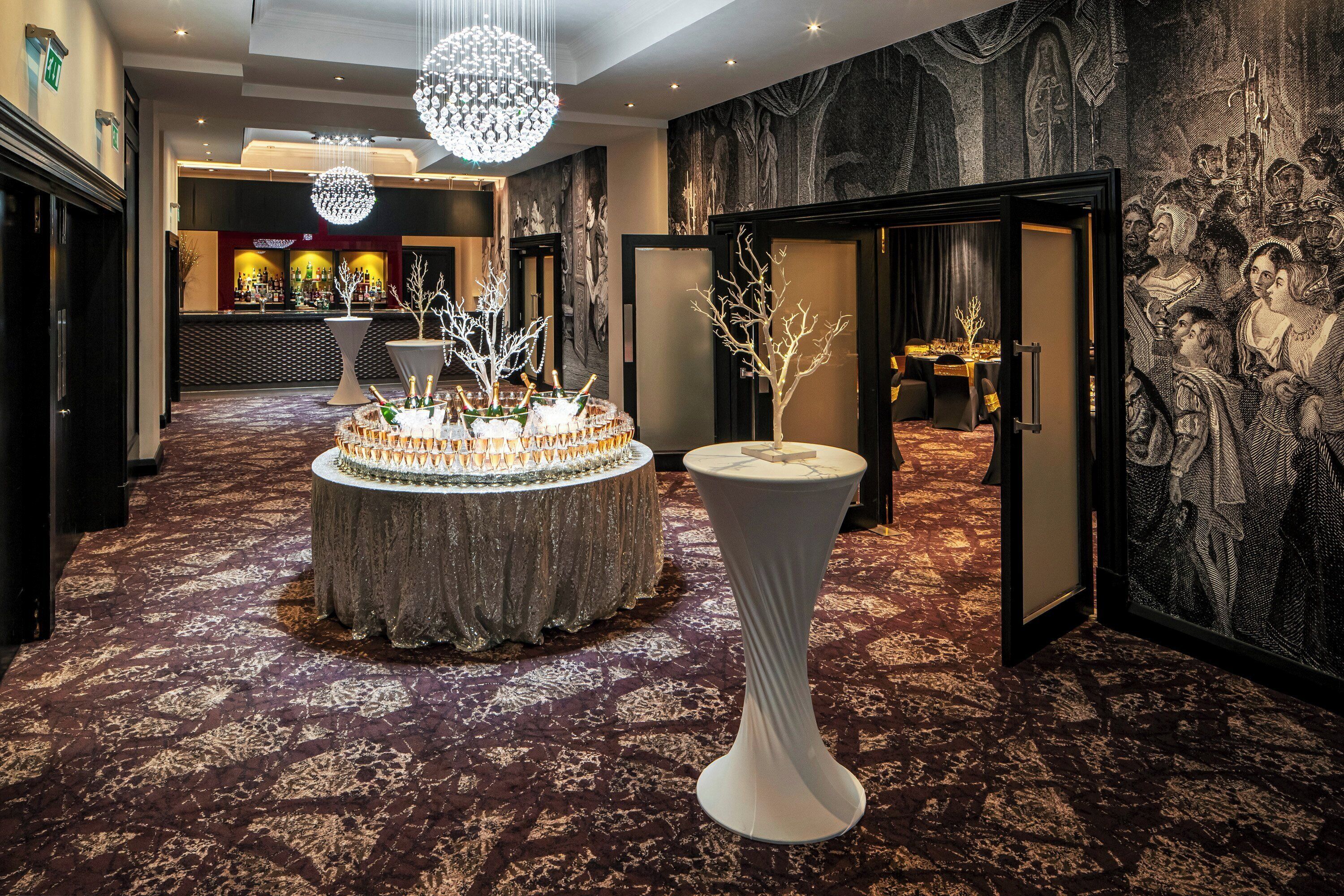 A lobby with a round table surrounded by chairs, a tall white pillar, and a chandelier.