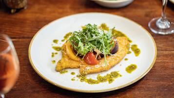 A plate of food with greens, tomatoes, and a sauce on a wooden table.