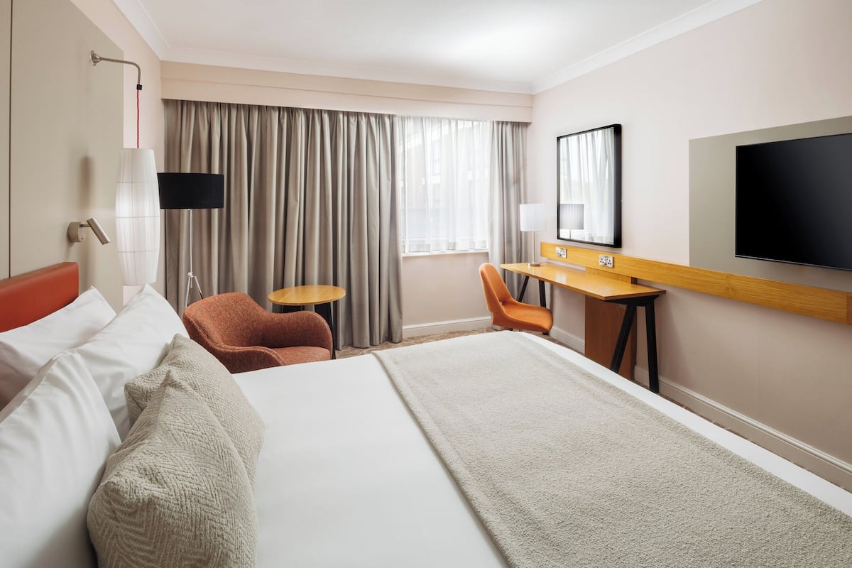 A hotel room with a large bed, a desk, a chair, a TV, and a window with curtains.