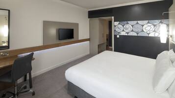 Una camera d'hotel con un letto, una scrivania con una sedia, una televisione e un muro decorato.