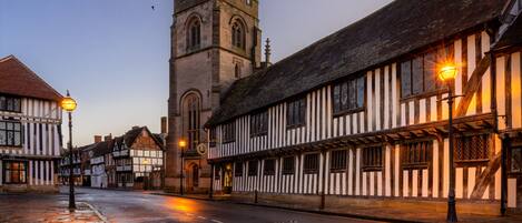 A historic street with traditional half-timbered buildings, a prominent church tower, and a cobblestone street.