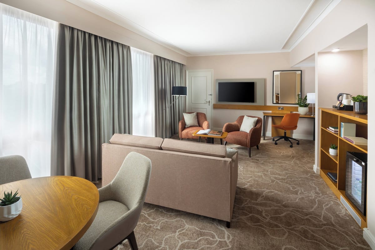 A hotel room with a sofa, armchairs, a desk, a TV, and a bookshelf.
