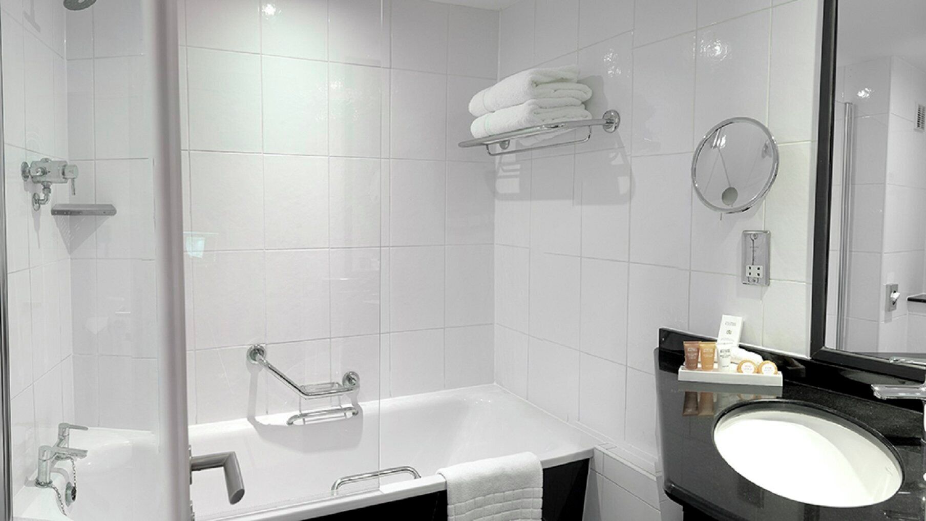 Une salle de bain moderne avec une douche à parois de verre, une baignoire sur pieds, un meuble-lavabo doté d’un plan de travail noir et un miroir.