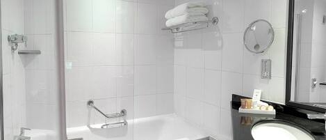 Un baño moderno con ducha envuelta en vidrio, una bañera independiente, un tocador con encimera negra y un espejo.